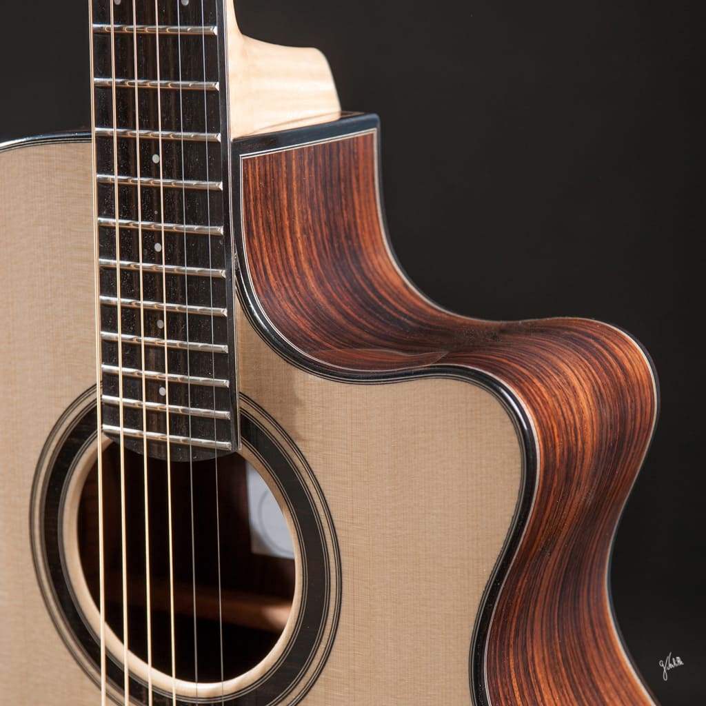 Photographe à Marseille Germain Verhille, photographie pour artisans et artisanat de métiers d’art : photo d’une guitare réalisée en studio, pensée comme une photo produit pour mettre en valeur le savoir-faire d’un luthier. L’image présente un gros plan de la guitare, révélant la table d’harmonie claire, le pan coupé en bois sombre aux veines élégantes, ainsi que les détails fins du manche et de la rosace, le tout mis en valeur par un fond sombre, noir, qui accentue la qualité artisanale de la pièce.