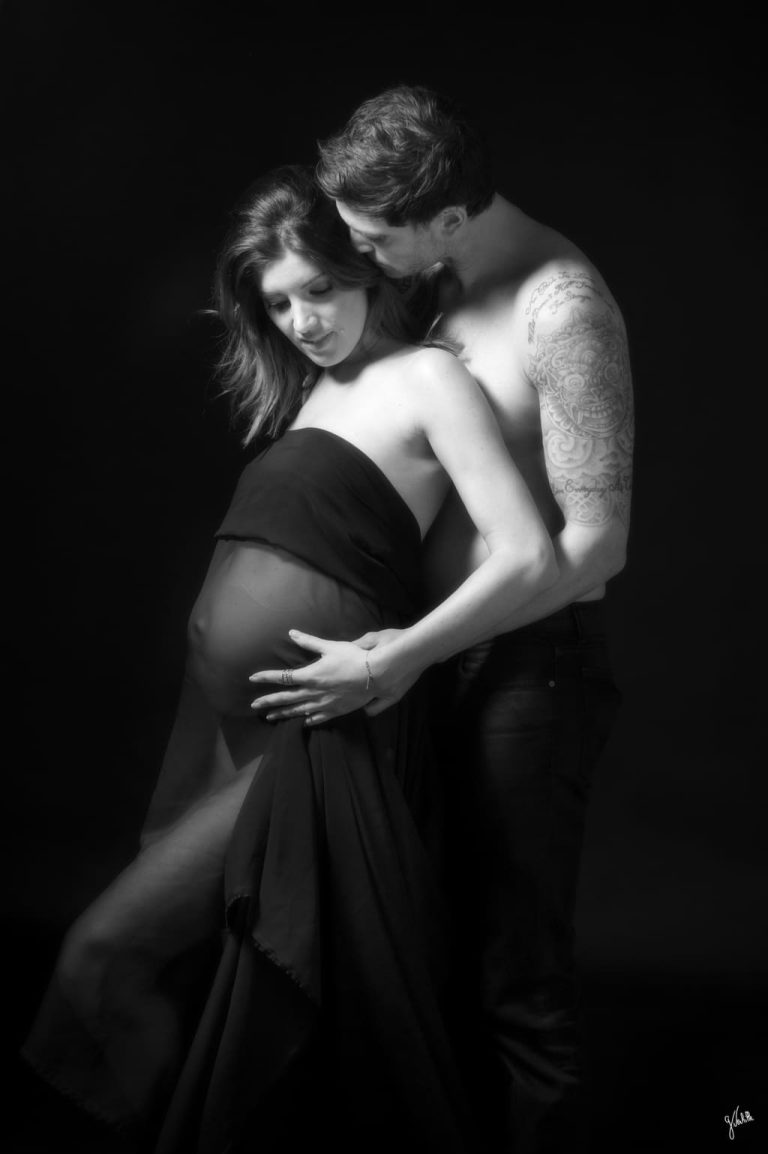 Photographe grossesse Marseille 14 hotographe de grossesse à Marseille – portrait en noir et blanc d’un couple en studio photo, réalisé lors d’un shooting photo grossesse. La femme enceinte, accompagnée de son compagnon, pose tendrement dans une lumière intimiste, créant une atmosphère douce et élégante. Cette séance photo en couple met en valeur le ventre rond de la future maman à travers une prise de vue soignée avec éclairage professionnel. Le photographe professionnel capture ici l’essence de la maternité, entre amour, complicité et préparation de séance photo. Une photographie de famille pleine d’émotion, pensée comme un souvenir inoubliable et destinée à enrichir un album photo de grossesse.